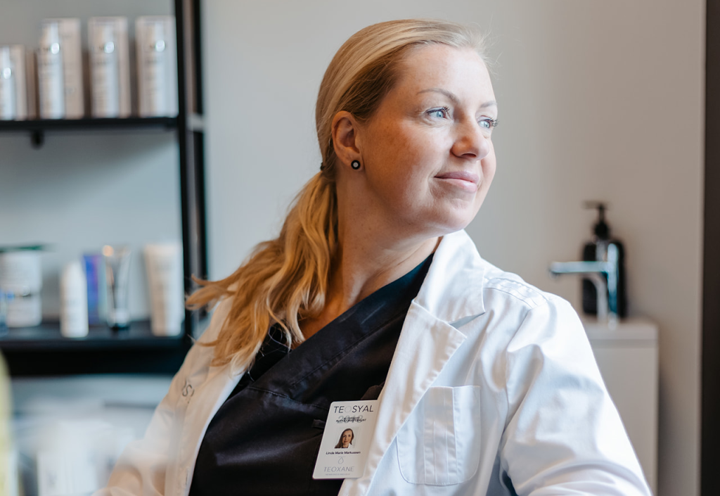 Sykepleier Linda Markussen i uniform ser ut mot siden og smiler